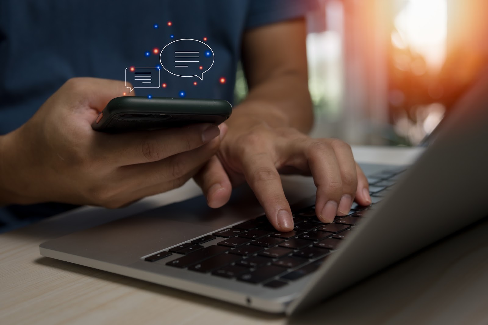 Person using a smartphone and laptop with chat message icons representing digital communication.