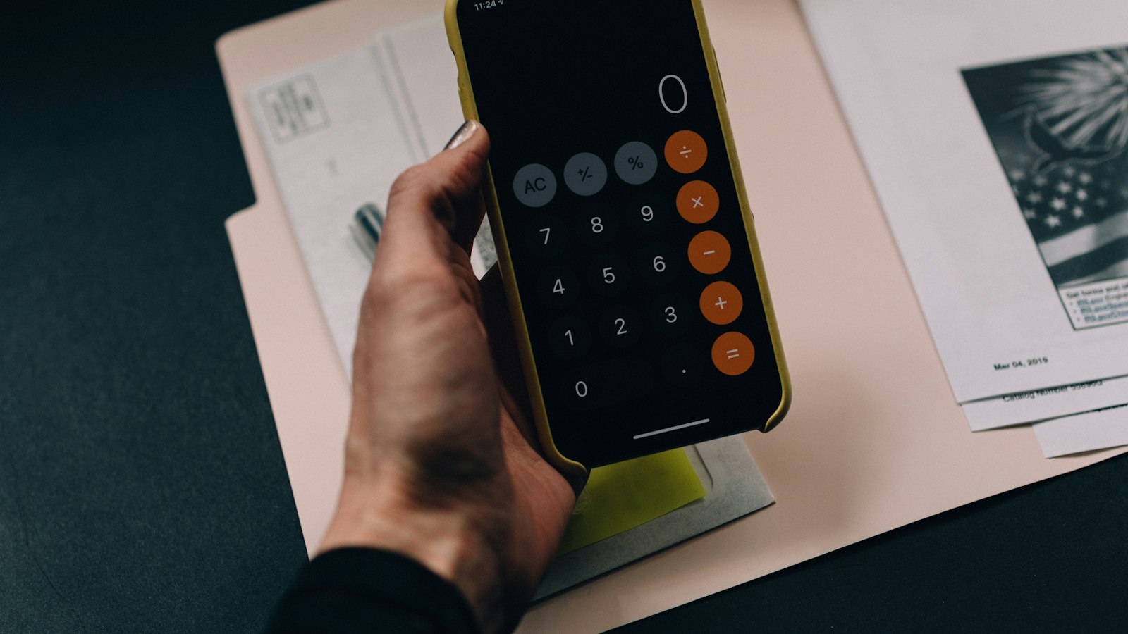 A person using a phone calculator beside printed documents