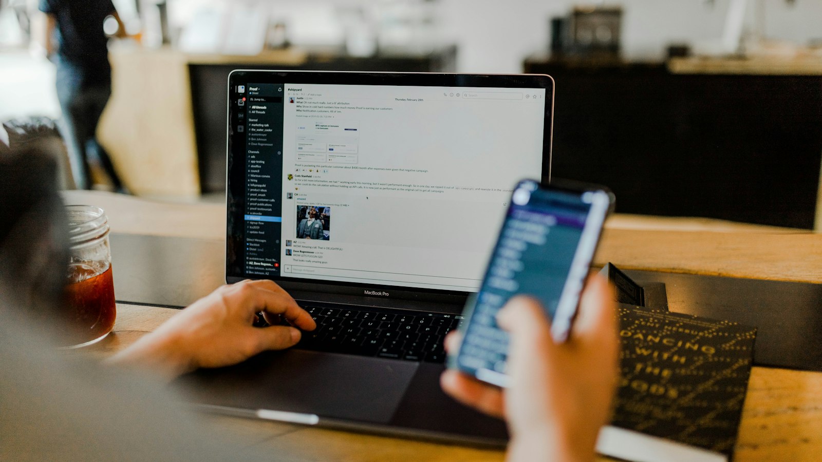 A person using a chat app on a laptop while holding a smartphone in an office