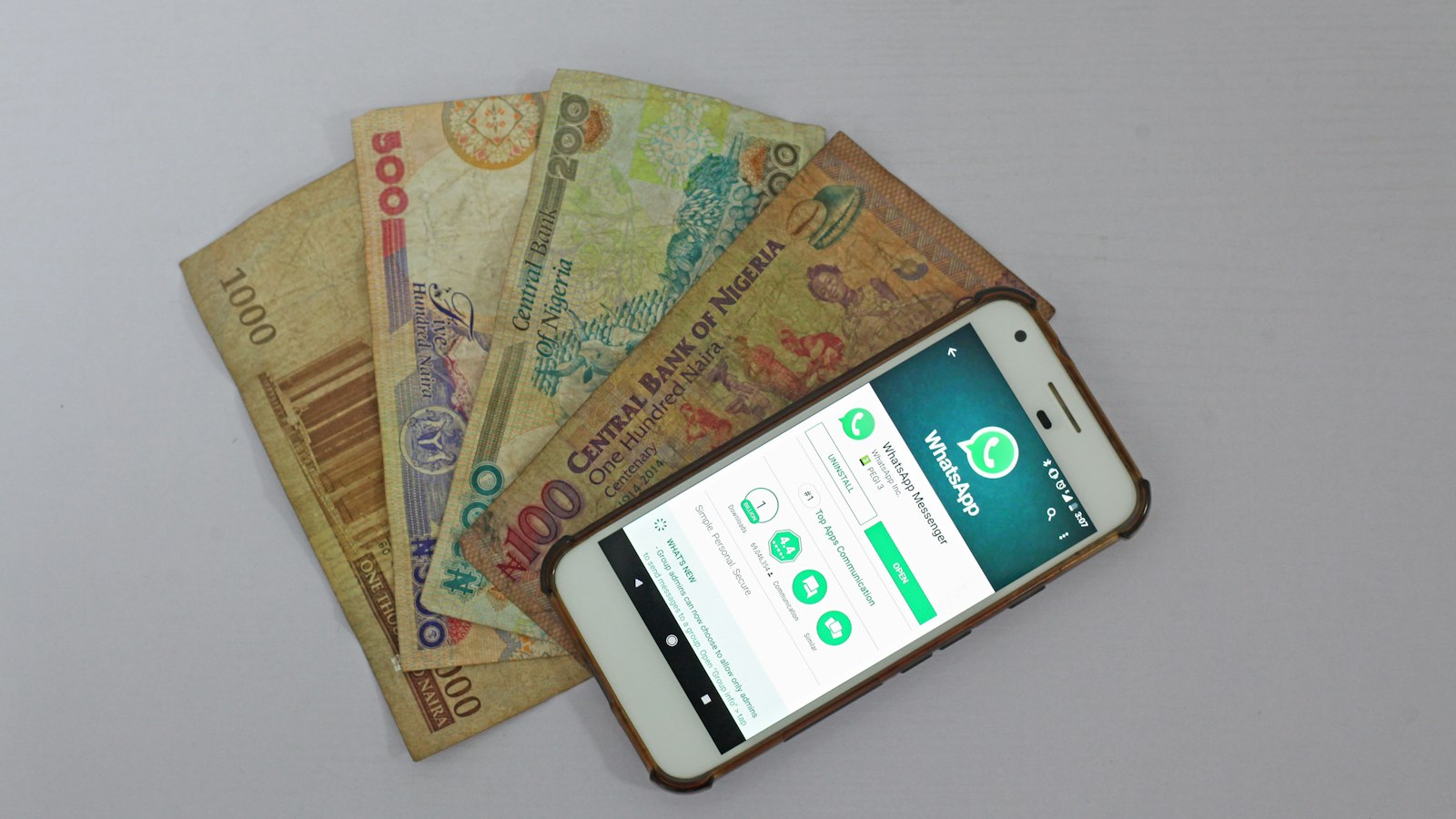 A smartphone showing WhatsApp above a fan of banknotes